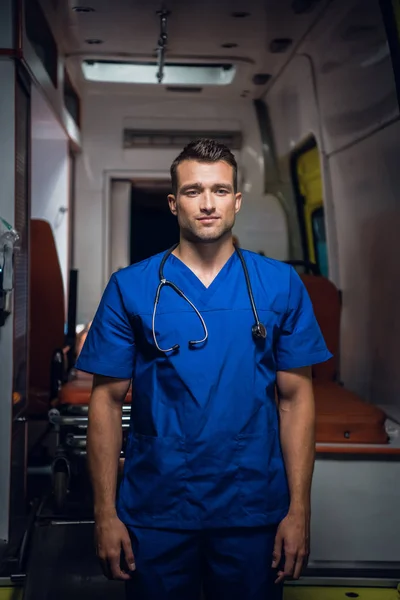 Jovem médico se levanta e olha para a câmera no carro da ambulância — Fotografia de Stock