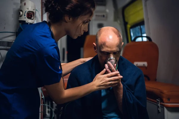 Perawat berseragam memegang masker oksigen pada pria yang duduk di selimut — Stok Foto
