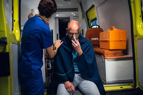 Enfermera de pie con el hombre que se sienta en la máscara de oxígeno en la manta en el coche de la ambulancia — Foto de Stock