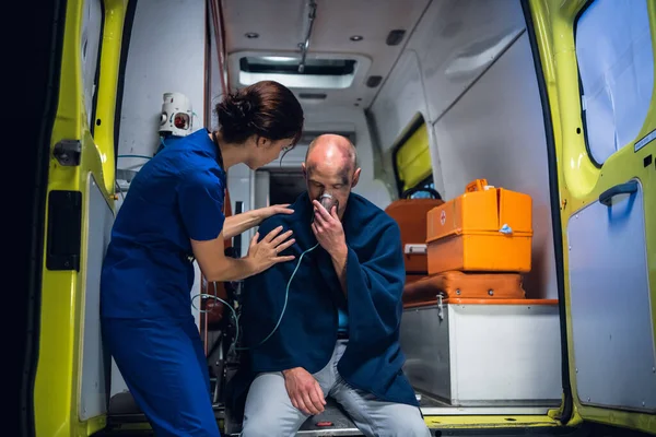 Врач в медицинской форме стоит рядом с человеком, который сидит в кислородной маске в одеяле — стоковое фото