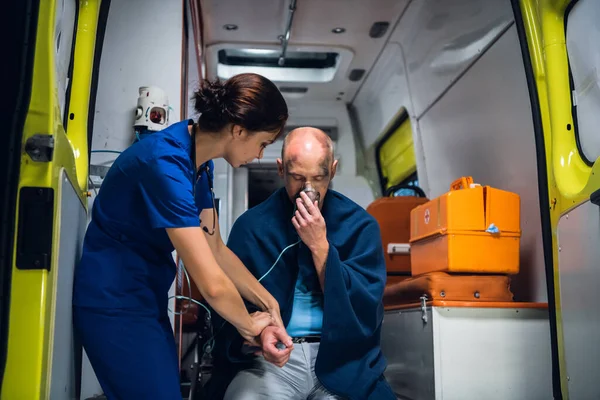 El hombre se sienta en manta con máscara de oxígeno, el médico de uniforme sostiene su mano —  Fotos de Stock