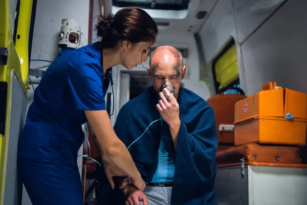 El hombre se sienta con máscara de oxígeno, la joven enfermera de uniforme está con él — Foto de Stock