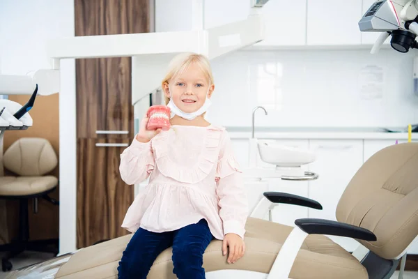Niña sonriendo y jugando con dentaduras postizas, en el consultorio dental — Foto de Stock