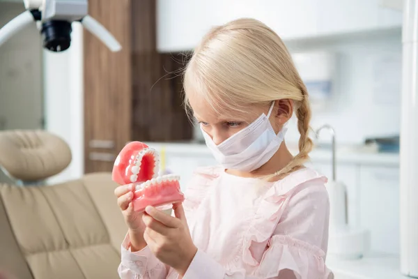 Un pequeño dentista con máscara médica inspeccionando dientes artificiales — Foto de Stock