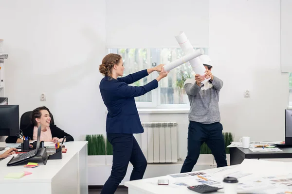 オフィスの真ん中で即興の剣を越えた同僚を笑っている若い女性 — ストック写真