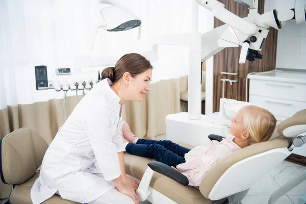 Uma criança pequena sentada no consultório odontológico com um médico conversando com ela — Fotografia de Stock