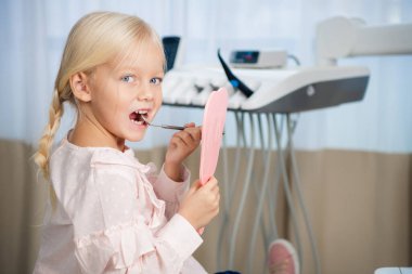 İnsanlar, tıbbi, stomatoloji ve sağlık hizmetleri konsepti - Küçük kız diş aynaları yardımıyla dişlerini inceliyor