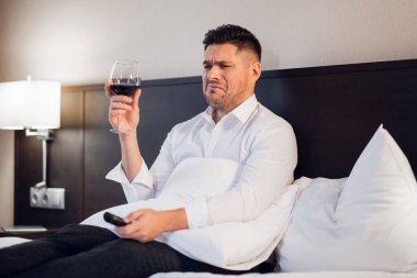 Yatağında bir kadeh şarapla sarhoş bir adam, pembe dizi izleyip ağlıyor.