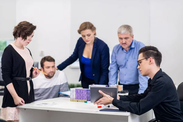 Un joven mostrando una presentación a sus colegas en la reunión usando su tableta y los modelos de casas — Foto de Stock