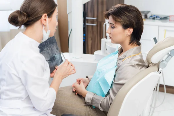 Μια όμορφη οδοντίατρος που δείχνει μια ακτινογραφία στον ασθενή της και εξηγεί κάτι. — Φωτογραφία Αρχείου