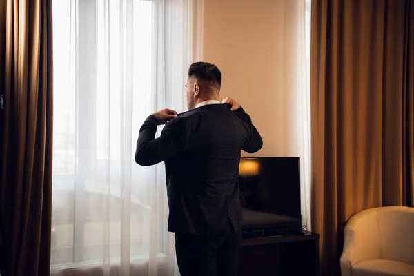 Νεαρός όμορφος επιχειρηματίας προσαρμόζει το σακάκι του ντύνεται στην πολυτελή σουίτα του ξενοδοχείου του προετοιμάζεται για μια συνάντηση κατά τη διάρκεια του επαγγελματικού του ταξιδιού — Φωτογραφία Αρχείου