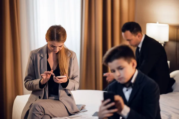 Gadget addiction concept. A family of three on a hotel bed, everyone is on their phone