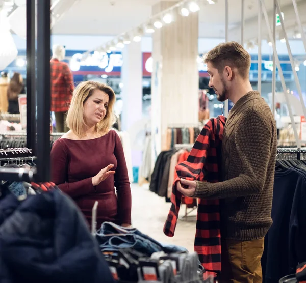 Junges Paar kauft Kleidung in einer Männerabteilung ein, das Mädchen mag das Hemd nicht, das ihr Freund ausgesucht hat — Stockfoto