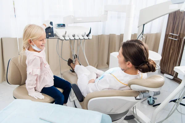 Doświadczony dentysta pozwala dziewczynie bawić się w jej biurze, aby nawiązać z nią kontakt, aby ją pocieszyć przed badaniem. — Zdjęcie stockowe