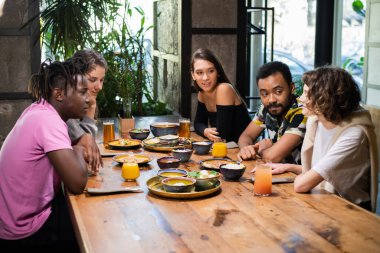 Bir kafede çok kültürlü bir grup genç, Asya yemeği yiyor, kokteyl içiyor, sohbet ediyorlar.
