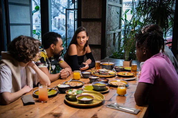 Een groep vrienden zit aan de tafel in een café, chatten, een leuke tijd hebben — Stockfoto