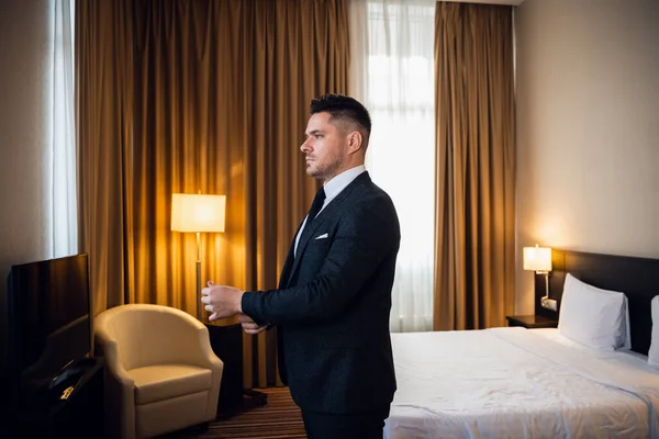 Ένας σοβαρός νεαρός επιχειρηματίας κοιτάζει αλλού με αυτοπεποίθηση, φτιάχνει τις χειροπέδες στο δωμάτιο του ξενοδοχείου του, ετοιμάζεται να βγει έξω. — Φωτογραφία Αρχείου