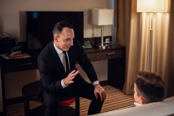 Um pai num fato formal a contar uma história ao seu filho num quarto de hotel — Fotografia de Stock