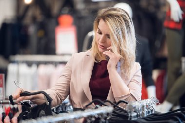 Modern kadın kıyafet alışverişi yapıyor ve akıllı telefonuyla konuşuyor.
