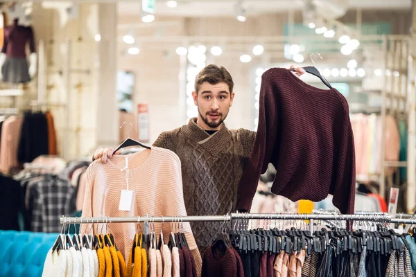 Молодой человек помогает своей девушке найти подходящий свитер в магазине одежды — стоковое фото