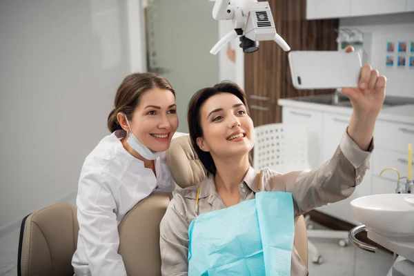 Una selfie inusual. Fotografía de una mujer sonriente tomando una selfie con su dentista después de su tratamiento médico — Foto de Stock