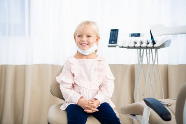 Dişçi muayenehanesinde güzel bir bayan çocuk kameraya bakıyor ve dişlek bir gülümsemeyle gülümsüyor.