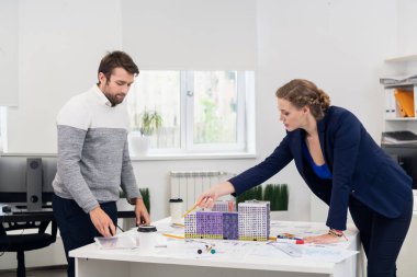 İş adamları ofiste toplantı yapıyor, inşaat projesiyle masanın etrafında duruyor ve bunu tartışıyorlar.