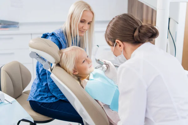 Uma dentista feminina está limpando os dentes das meninas com uma ferramenta especial, a menina está olhando para o médico — Fotografia de Stock