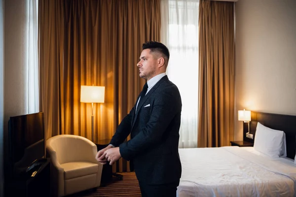 Νεαρός όμορφος επιχειρηματίας προσαρμόζει το σακάκι του, ντύνεται στην πολυτελή σουίτα του ξενοδοχείου του προετοιμάζεται για μια συνάντηση κατά τη διάρκεια του επαγγελματικού του ταξιδιού. Ένα κομψό, κομψό, αρρενωπό, με αυτοπεποίθηση, εστιασμένο στέλεχος — Φωτογραφία Αρχείου
