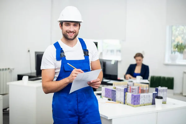 Ein junger lächelnder Bauarbeiter macht sich im Büro Notizen — Stockfoto