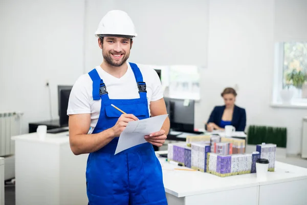 Um jovem trabalhador da construção sorrindo tomar notas enquanto no escritório — Fotografia de Stock