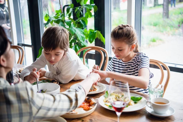 Twee kinderen met hun moeder die eten delen tijdens het eten. — Stockfoto