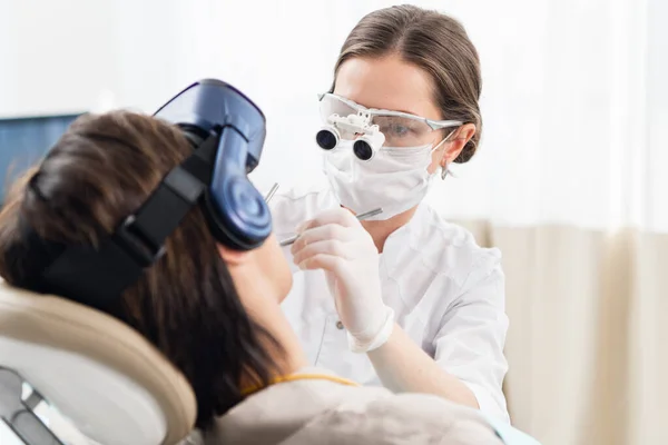Modern bir diş tedavisi gören genç bir kadın hoş olmayan diş işlemlerinden dikkatini dağıtmak için VR gözlük kullanıyor. — Stok fotoğraf