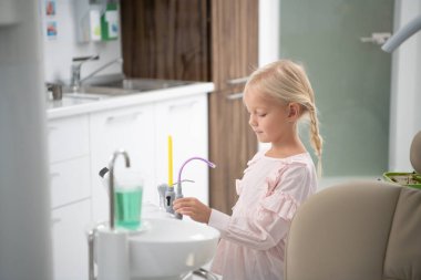 Diş kliniğindeki küçük sarışın kız. Steril su dolu bir fincan.