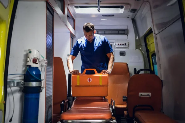 Üniformalı genç doktor çantasını ambulans arabasına koyar.