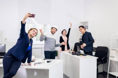 Çalışanlar ofiste eğleniyor, poz veriyor ve selfie çekiyorlar.