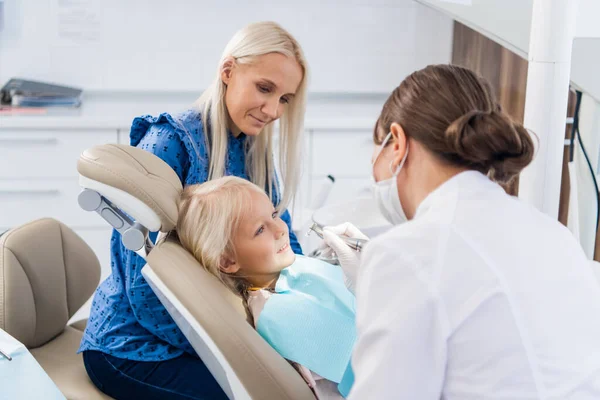 Ο οδοντίατρος καθαρίζει τα δόντια των κοριτσιών με ένα ειδικό εργαλείο, το κορίτσι κοιτάζει το γιατρό — Φωτογραφία Αρχείου