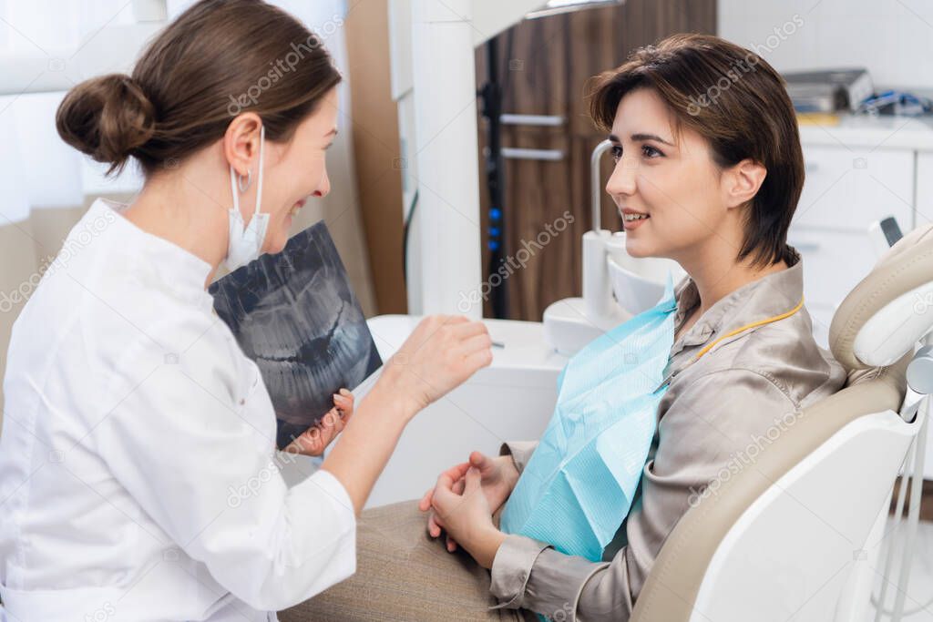A young dentist shows her patient an x-ray and explains somethin