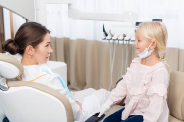 Bir dişçi kliniğinde oturmuş gülümseyen küçük bir kız.