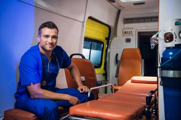 Pasante joven sentado en un coche de ambulancia y sonriendo —  Fotos de Stock