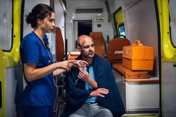 Coche de ambulancia, una enfermera joven le está dando una máscara de oxígeno a un hombre herido en una manta — Foto de Stock