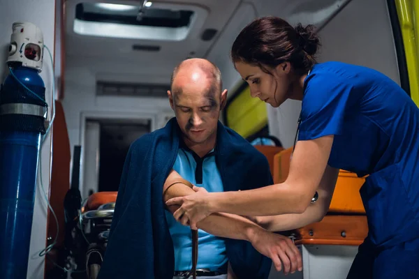 Женщина в синей форме обертывает жгут вокруг руки раненого мужчины — стоковое фото