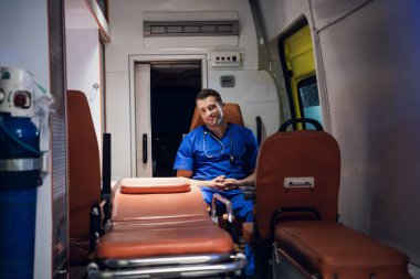 Ambulans arabasında oturan, birine gülümseyen pozitif erkek sağlık görevlisi.