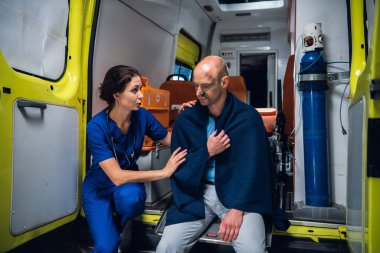 Ambulans arabası, battaniyeli bir adamla konuşan hemşire, onu sakinleştirmeye çalışıyor.