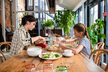 Anne ve kızı bir kafede pizza paylaşıyor.