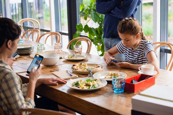 Moeder en dochter zitten aan tafel op hun telefoon — Stockfoto