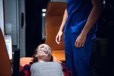 Bir kadın, sedyede, üzerinde öküz maskesi olan ve mavi üniformalı sağlık görevlisine bakan bir kadın.