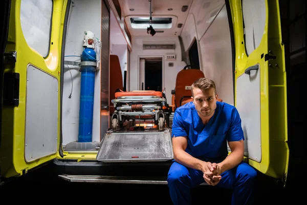 Un homme sérieux sous une iniforme médicale assis à l'arrière d'une ambulance — Photo