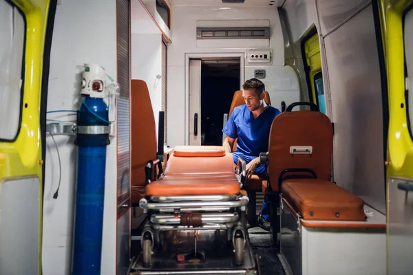 Молодой парамедик в синей форме сидит в машине скорой помощи — стоковое фото