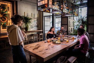 Genç ve güzel bir kız bir kafede arkadaşlarına bir şeyler anlatıyor.